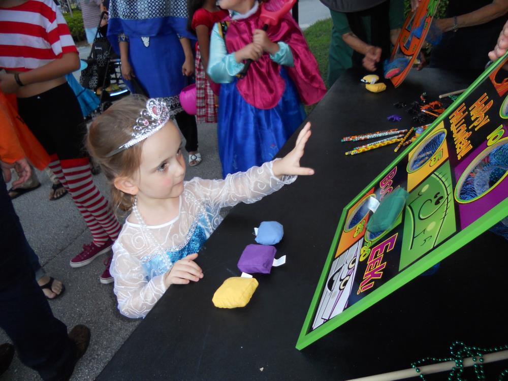 Girl dressed as Elsa trying to throw bean bags through holes in cardboard rectangle on table